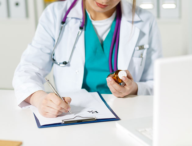 En kvinnelig lege ved skrivebordet hennes fyller ut et skjema.