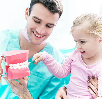 Dentisti i tregon një pacienti se si të lajë dhëmbët si duhet.